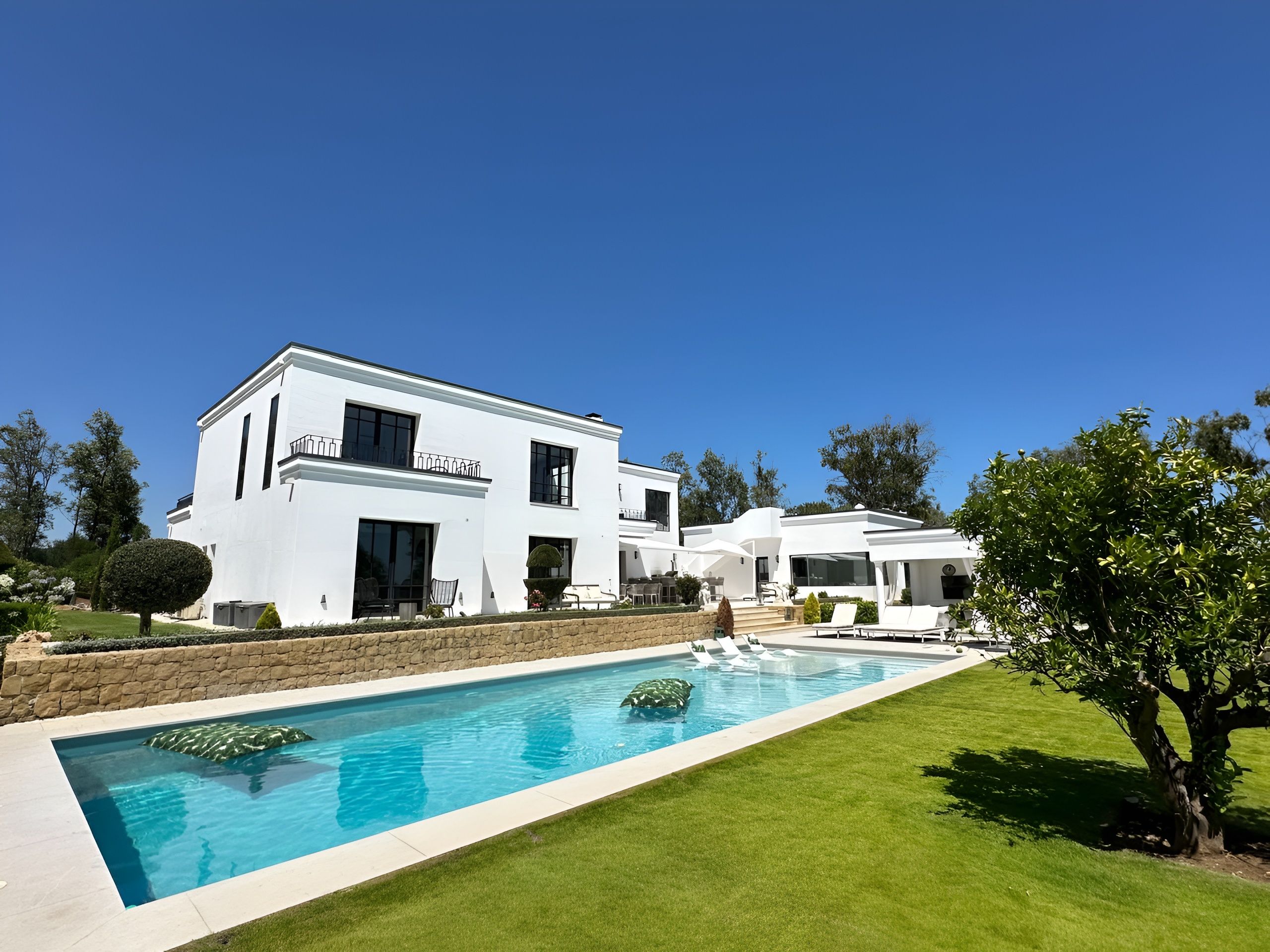 Contemporary white villa with black steel glazing, long pool, sun ledge and lawn in La Reserva de Sotogrande