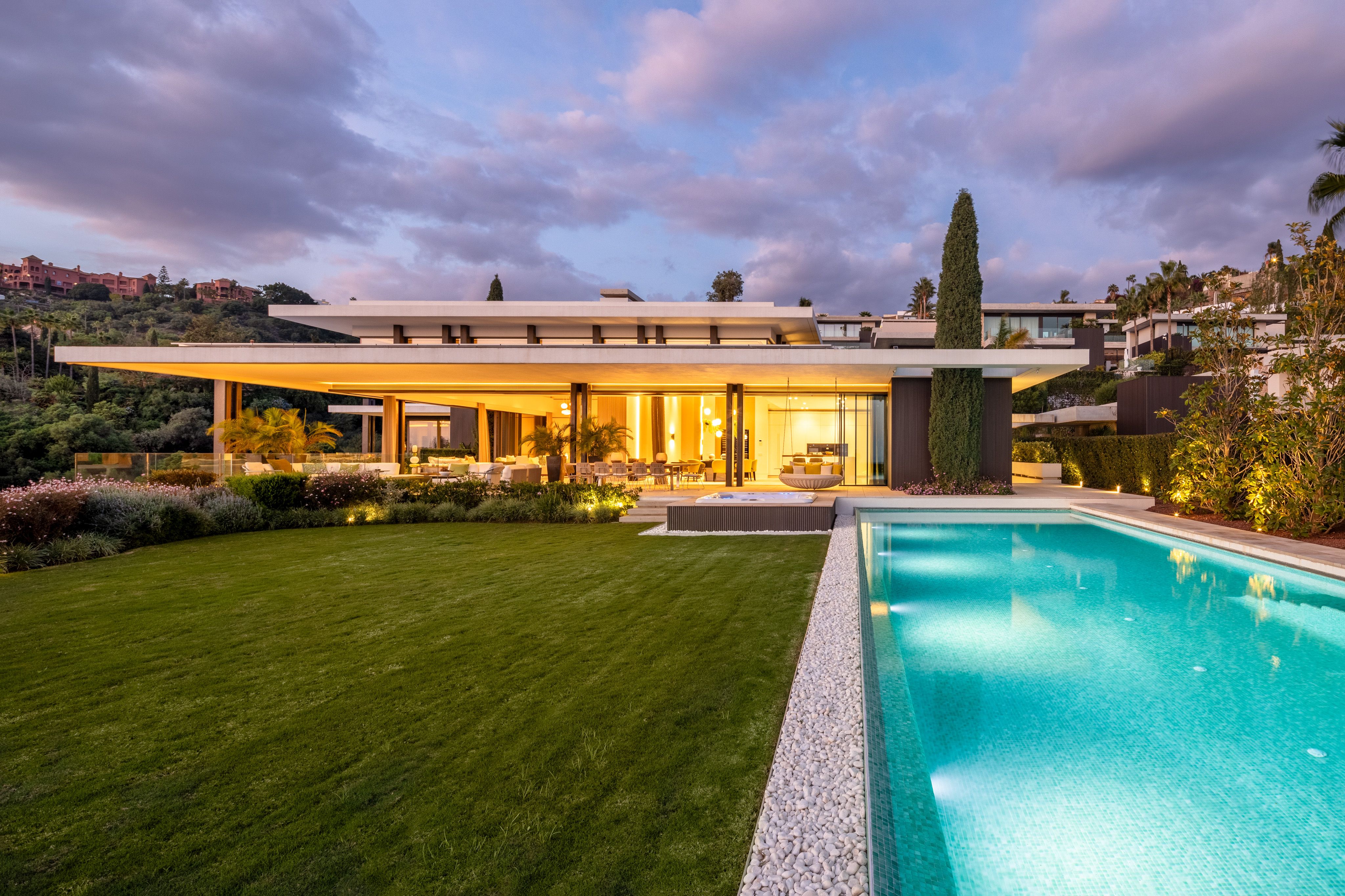 Dusk exterior view of The Hills 1 villa with private pool, landscaped garden and illuminated terrace in La Quinta, Benahavis.