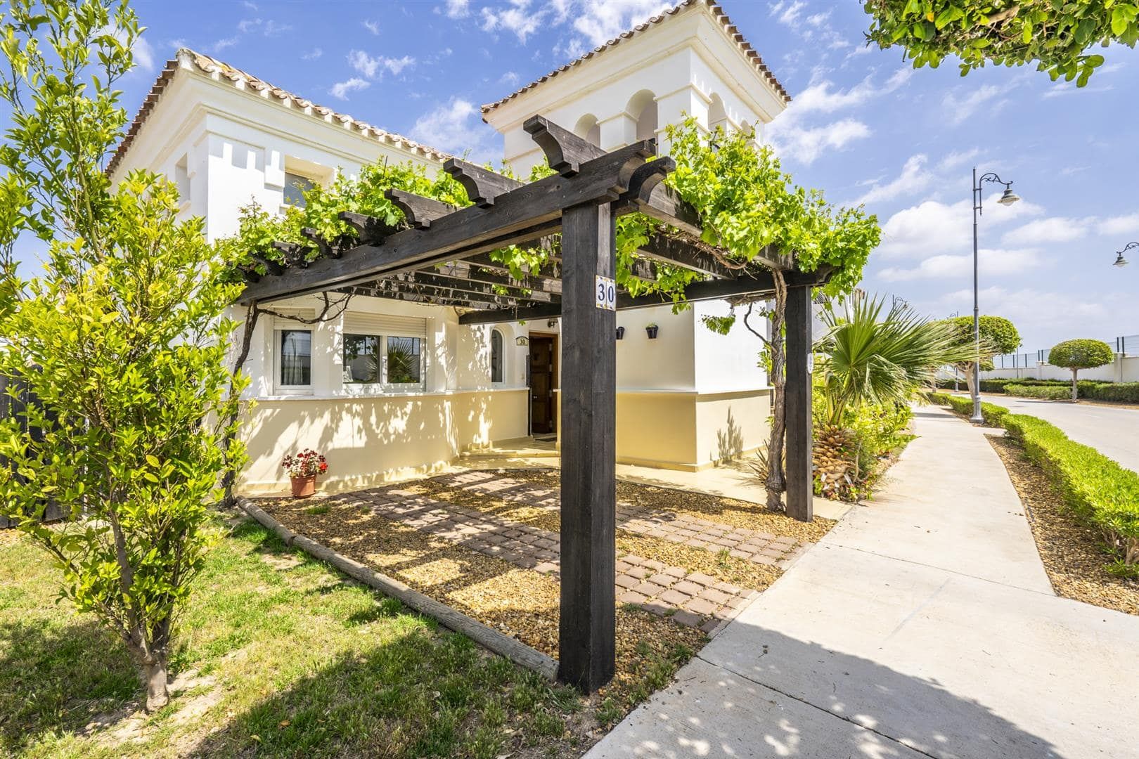 Villa entrance, pergola and landscaped path under blue sky