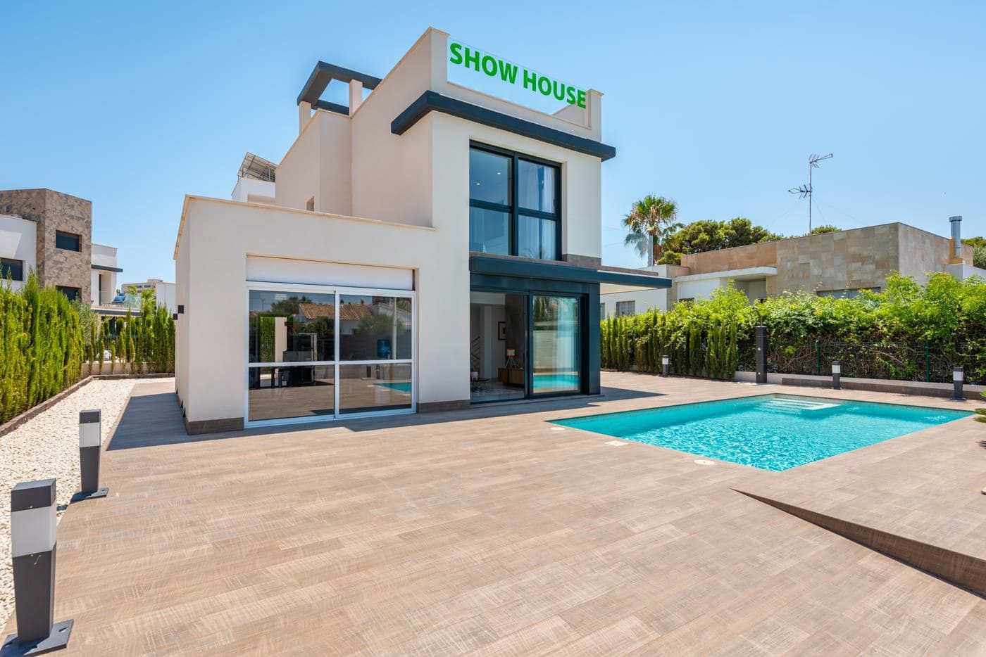 Photograph of a contemporary white show house beside a swimming pool and broad tiled terrace in daylight