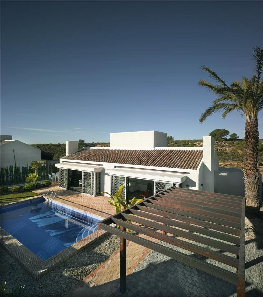 Elevated daylight view of a white single-storey villa beside a swimming pool and timber pergola