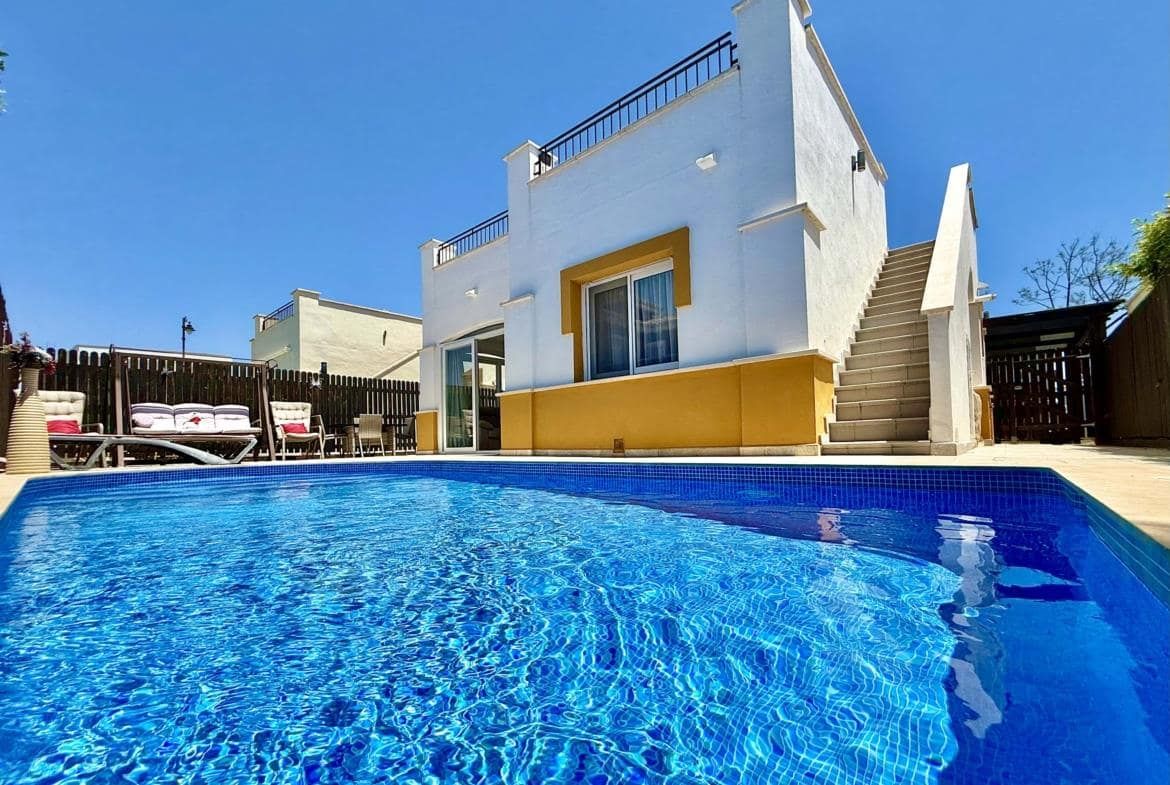 Low-angle daylight view across a swimming pool towards a white villa facade and exterior stairs