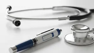 An injectable medication pen sitting on a clean surface next to a stethoscope, representing pharmaceutical medical treatment.