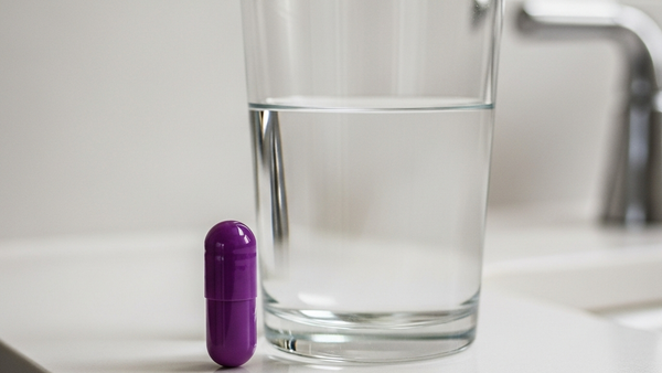 A purple capsule of Nexium medication resting on a bathroom counter next to a glass of water, with soft lighting and no text visible.