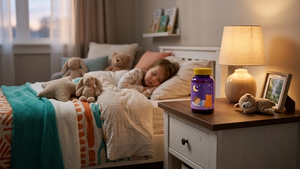 A bottle of pediatric gummy melatonin supplements resembling Mommy's Bliss packaging sitting on a nightstand next to a child's bed.