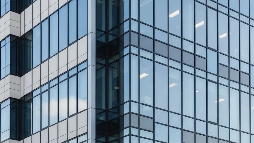A modern office building exterior with glass windows reflecting the sky, representing a corporate workplace environment.