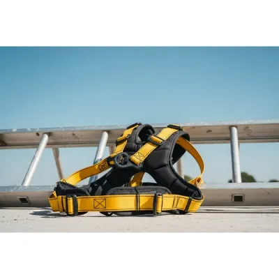 A pair of yellow heavy-duty fall protection harnesses lying next to a metal roof ladder on a construction site with a clear blue sky in the background.