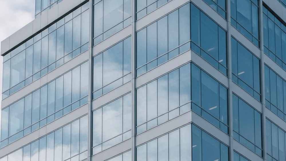 A modern corporate office building with glass windows reflecting the sky, representing an environment under federal investigation.
