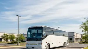 A large white luxury coach bus parked in a quiet commercial parking lot during the day, representing the transportation industry.