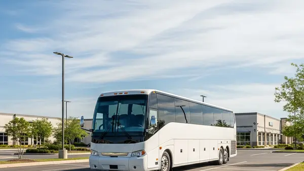 A large white luxury coach bus parked in a quiet commercial parking lot during the day, representing the transportation industry.