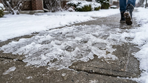 A close-up of a thick patch of jagged ice on a concrete sidewalk during a cold winter day with snow on the edges.