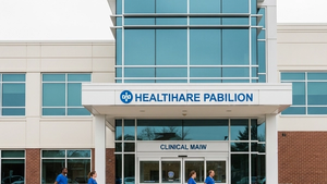A modern healthcare pavilion exterior with medical staff in scrubs walking near the entrance of a clinical building.