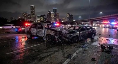A night scene of a Houston highway with emergency lights reflecting on the road near the charred remains of two vehicles involved in a head-on collision.