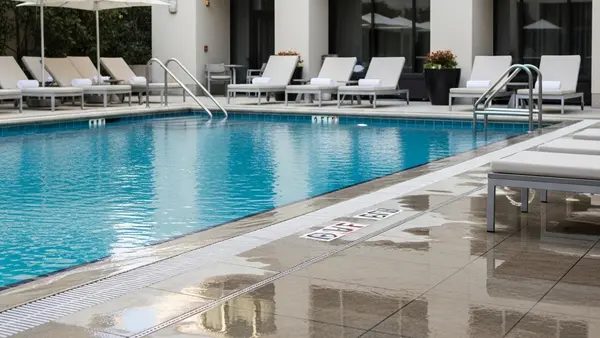 A luxury hotel swimming pool area with lounge chairs and blue water, showing a wet tile floor near the edge without any safety signage.