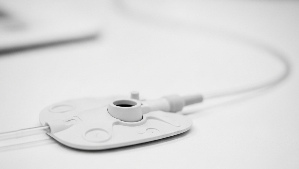 A close-up of a medical port device with a thin catheter tube, resting on a clean clinical surface, emphasizing the synthetic material and structural design.