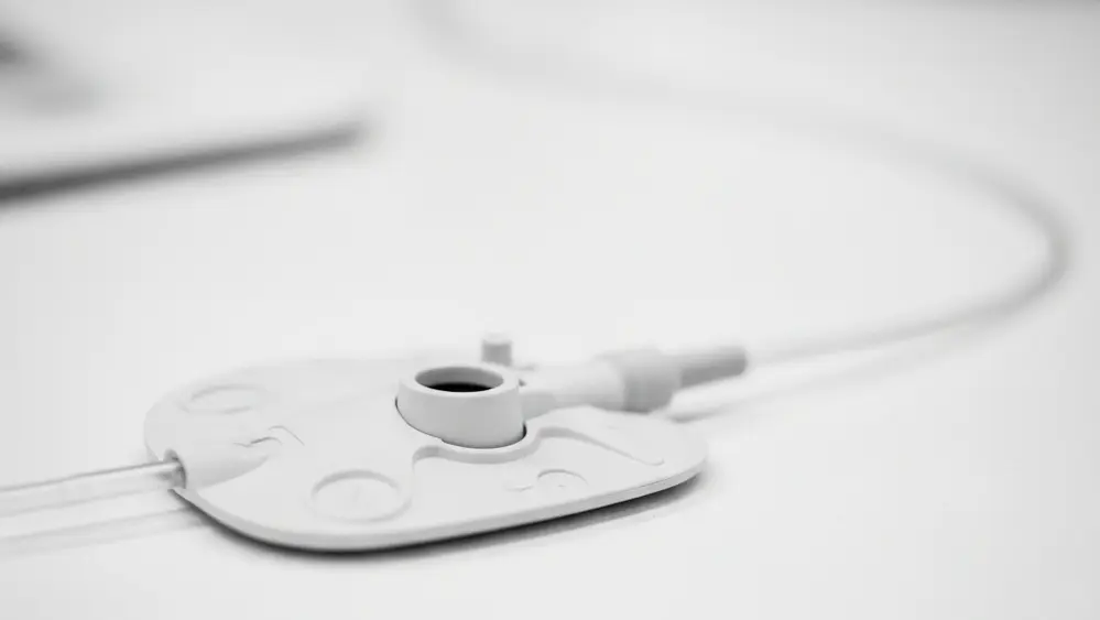 A close-up of a medical port device with a thin catheter tube, resting on a clean clinical surface, emphasizing the synthetic material and structural design.
