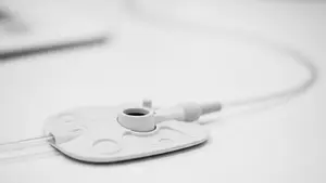 A close-up of a medical port device with a thin catheter tube, resting on a clean clinical surface, emphasizing the synthetic material and structural design.