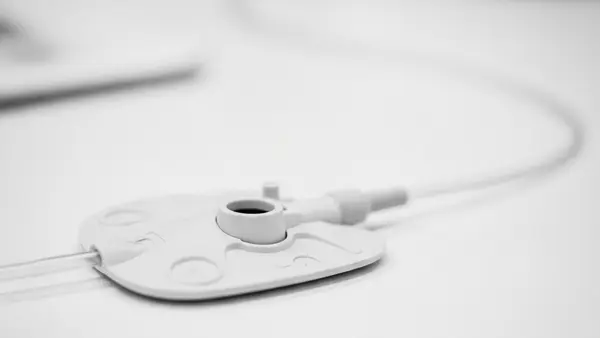 A close-up of a medical port device with a thin catheter tube, resting on a clean clinical surface, emphasizing the synthetic material and structural design.