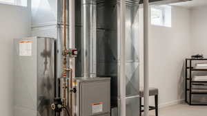 A modern residential furnace installed in a home basement with a gas pipe and exhaust vent visible.