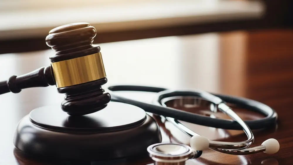 A close-up of a wooden gavel resting on a desk next to a stethoscope, symbolizing the intersection of the legal and medical systems.