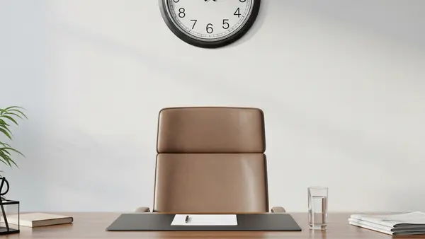 A large, professional wooden desk in a quiet office setting, featuring an empty executive chair, a glass of water, and a classic analog clock on the wall, symbolizing years of service and the passage of time.