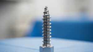 A close-up view of a metal spinal fusion pedicle screw resting on a blue surgical drape in a hospital setting.