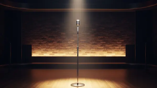 A brightly lit stage with a lone microphone stand in a comedy club setting, symbolizing the workplace environment involved in the legal settlement.