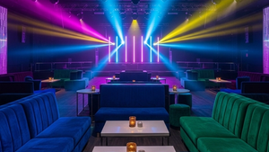 An interior view of a contemporary nightclub lounge with velvet seating and colorful stage lights, representing the entertainment industry environment.