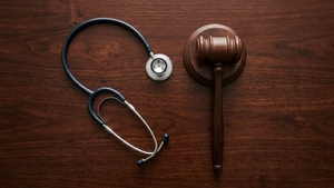 An overhead view of a stethoscope resting on a dark wooden surface next to a gavel, symbolizing the intersection of medicine and law