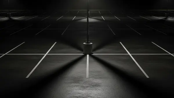 A dark commercial parking lot at night with a single flickering overhead light casting long shadows across empty parking spaces.