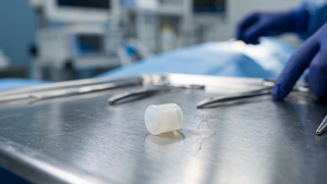 A close-up of a small, translucent synthetic cartilage plug designed for big toe implants resting on a metallic surgical surface