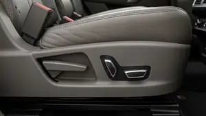 A detailed close-up of a modern SUV interior showing the mechanical hinge and power controls of a rear leather seat in a neutral-colored vehicle.