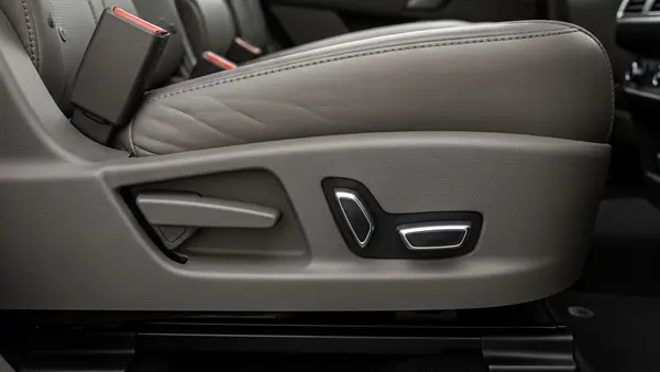 A detailed close-up of a modern SUV interior showing the mechanical hinge and power controls of a rear leather seat in a neutral-colored vehicle.