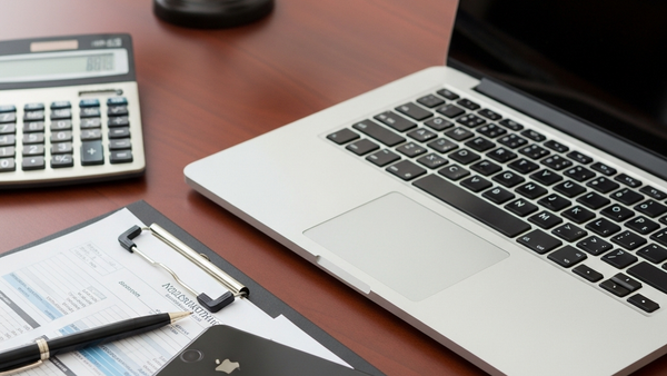 A sleek silver laptop and a high-end smartphone sitting on a mahogany office desk next to a calculator and professional financial documents.