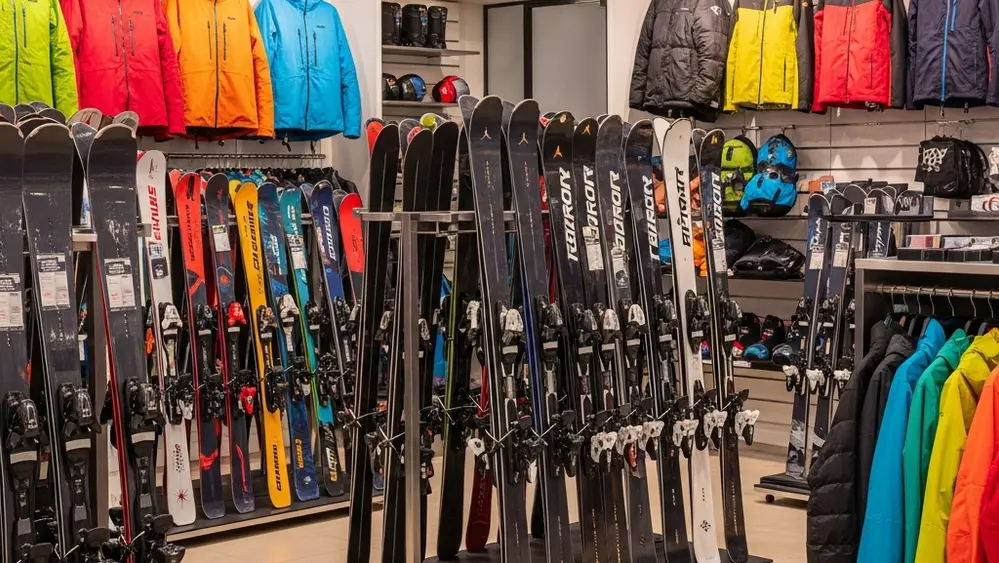 A variety of high-end winter sports equipment including skis, snowboards, and colorful outdoor jackets displayed in a modern, brightly lit retail showroom.