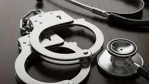 A close-up of metal handcuffs lying on a dark wooden surface next to a medical stethoscope, symbolizing the intersection of law and physical injury.