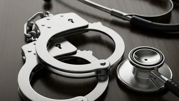 A close-up of metal handcuffs lying on a dark wooden surface next to a medical stethoscope, symbolizing the intersection of law and physical injury.