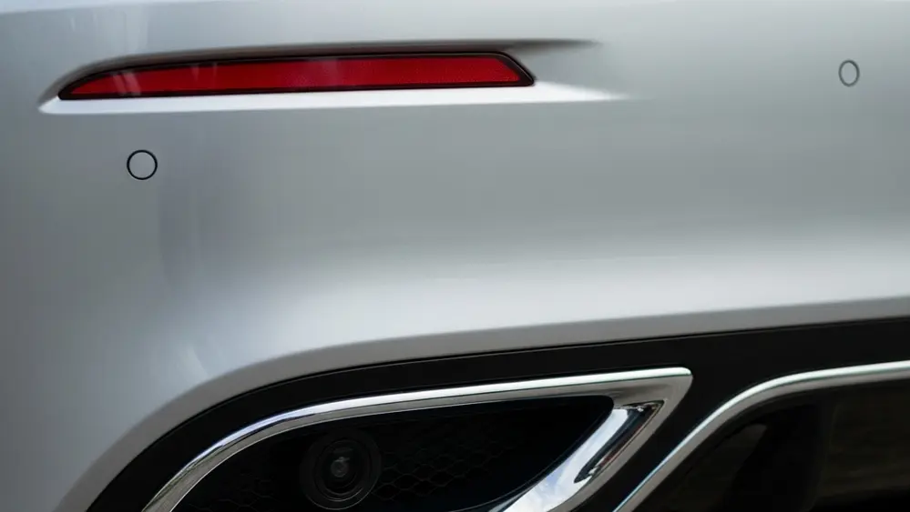 A close-up view of the rear bumper of a modern silver luxury sedan, focusing on a small circular camera lens integrated into the bodywork.