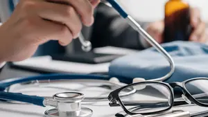 A close-up of a doctor's stethoscope resting on a desk next to a blurred-out medical folder and a pair of eyeglasses in a professional setting.