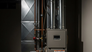 A modern residential gas furnace installed in a dimly lit basement utility room with metal ventilation pipes and copper gas lines.