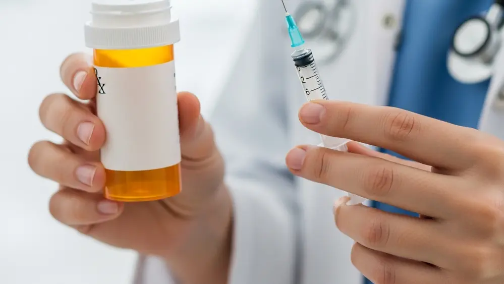 A close up of a medical professional's hands holding a prescription bottle and a syringe, representing pharmaceutical treatment.