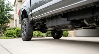 A modern pickup truck parked on a suburban driveway with a focus on the undercarriage near the rear fuel tank, shown without logos, signs, or text.