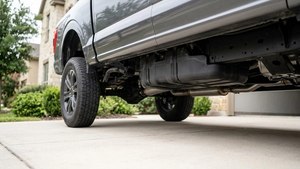 A modern pickup truck parked on a suburban driveway with a focus on the undercarriage near the rear fuel tank, shown without logos, signs, or text.