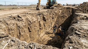An excavation site with deep dirt walls and no visible safety shoring or protection systems in place.