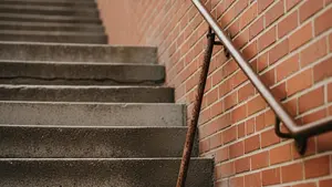 A steep outdoor concrete staircase with a rusted, detached handrail leaning against a brick wall.