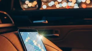 A smartphone with a rideshare map interface sitting on the leather seat of a car, with the glowing lights of a city visible through the window at night.