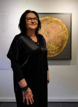 The artist in black beside a peach-coloured planet in gold-coloured metal leaf, a poem on the wall to her left.