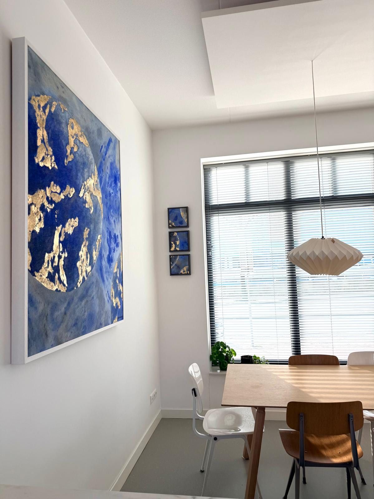 The same room from closer in: the blue and gold planetary painting on the left wall, the triptych by the window and the table below.