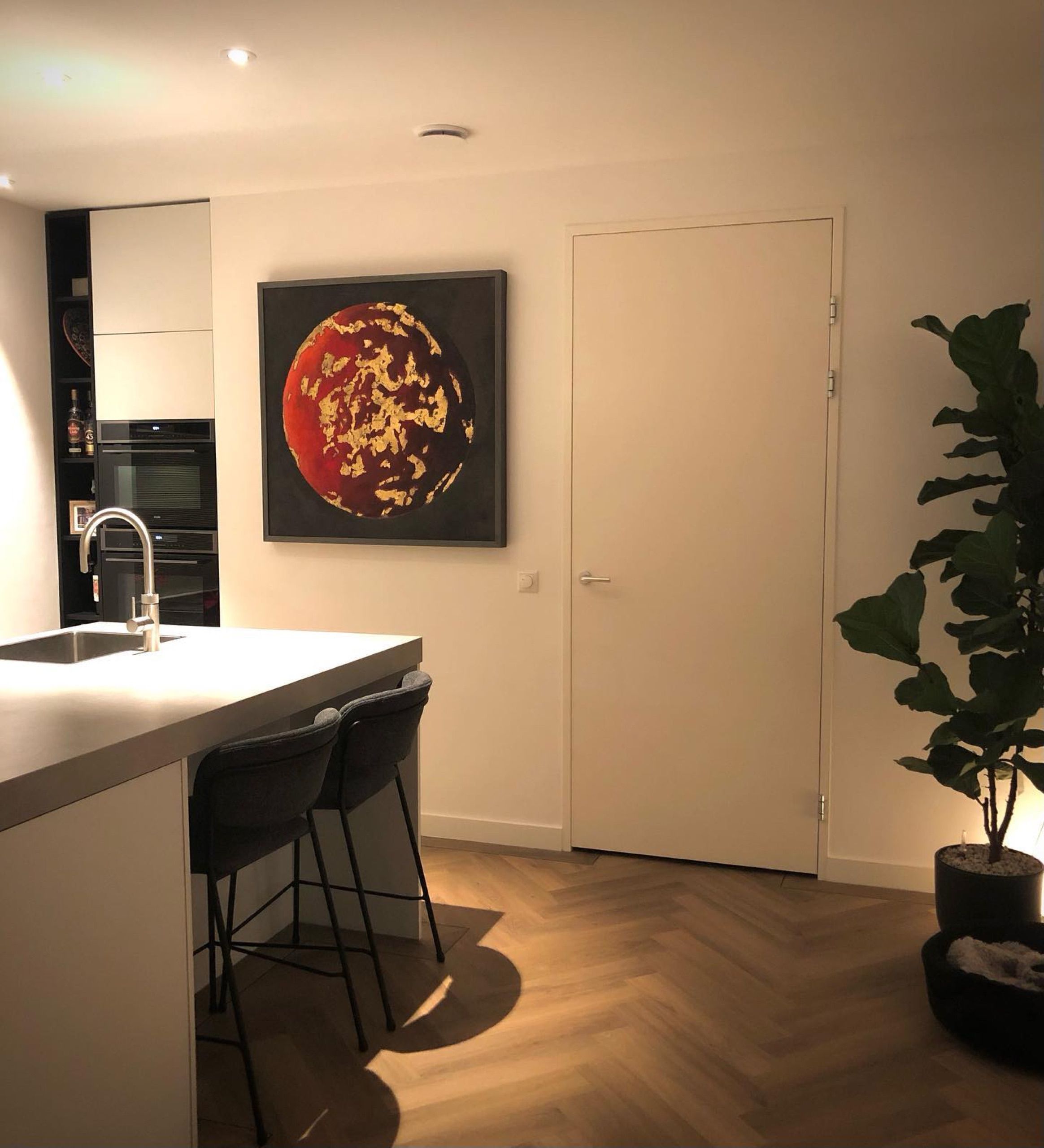 A red planet with gold-coloured metal leaf on a kitchen wall in evening light.
