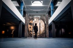 A visitor stands in front of Connected: five hanging panels that together form a moon in gold and grey.